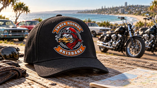 Ember Hounds Brisbane motorcycle club curved-brim cap prepared beside parked V-twin motorcycles for a coastal festival arrival.