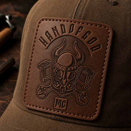 Rugged leather motorcycle club logo patch mounted on a brown canvas cap.