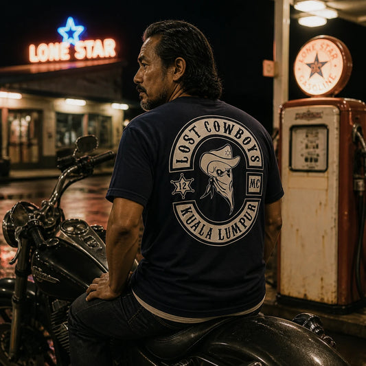Lost Cowboys MC rider in a roomy relaxed-fit short-sleeve club T-shirt at a vintage night gas station.
