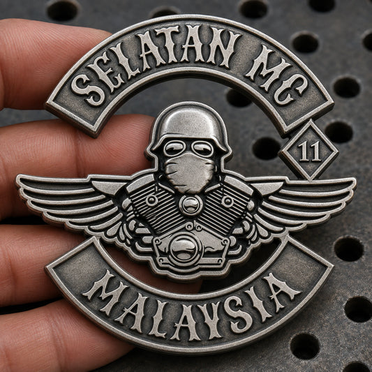 Connected antique silver motorcycle club pin with real open cut-outs between wing and engine details, held over a perforated workshop bench.