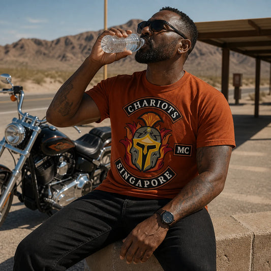 Chariots MC rider wearing a rust orange short-sleeve T-shirt with a large centered front emblem at a desert road stop.