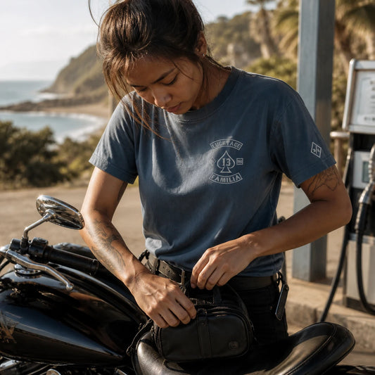 Luckyace MC rider securing a motorcycle bag in a softly draped faded blue 180 GSM everyday-weight club T-shirt at a coastal fuel stop.