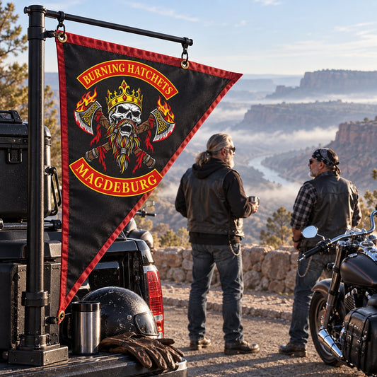Two American V-twin riders stand at a mountain turnout beside their custom motorcycle club triangle flag.