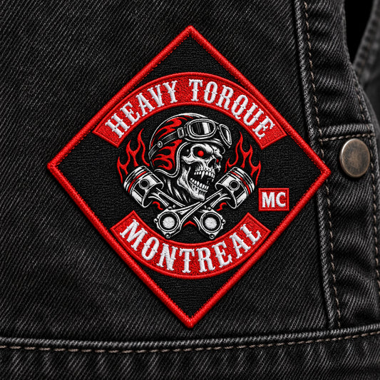 Small diamond-shaped embroidered identifier with neutral fictional initials for a motorcycle club, shown at black denim vest side panel.