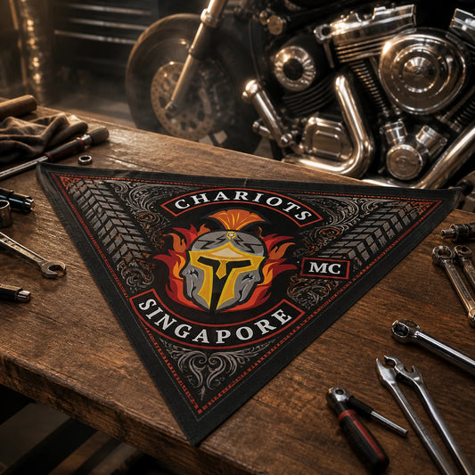 Custom motorcycle club bandana featuring the authorized Chariots MC identity in a timber workbench inside a custom-bike garage, triangle bandana beside hand tools and a softly blurred V-twin engine.