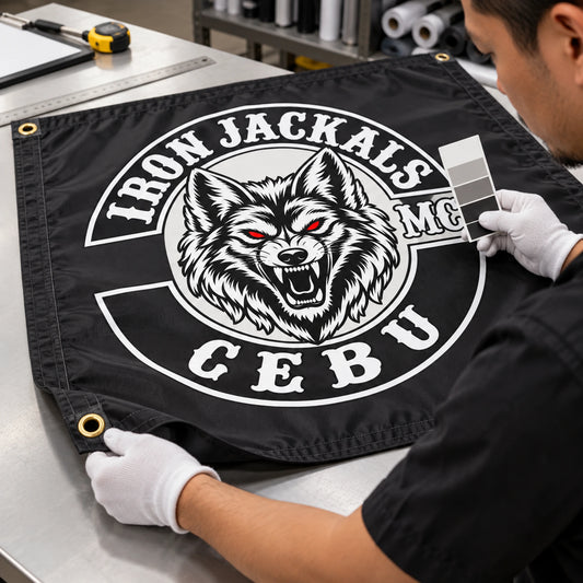 A print technician checks club colors, reinforced edges and grommets on a custom motorcycle club flag.