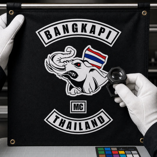 A gloved craftsperson inspects an accurately reproduced motorcycle club logo on a custom hanging flag.