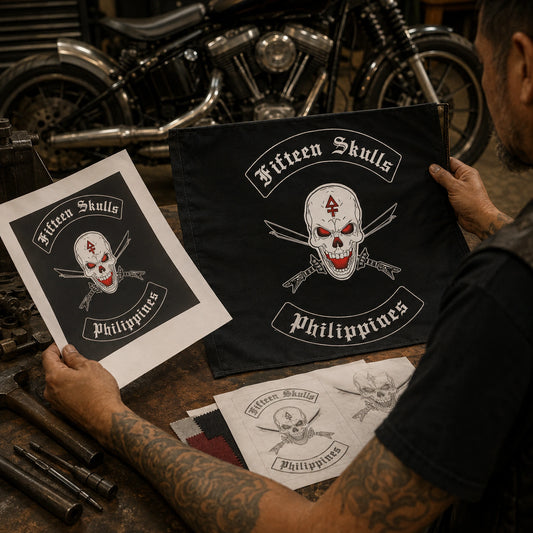 A motorcycle club art officer compares the authorized emblem with a custom flag mockup at a garage workbench.