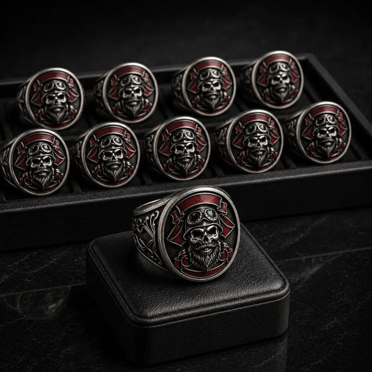 Approved custom motorcycle club ring displayed on a black leather pad with multiple matching skull rings arranged in a production tray behind it.