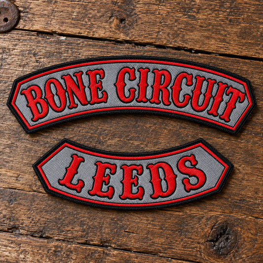 Custom-shaped embroidered name bar with restrained clipped corners, shown alone on textured leather without becoming a curved rocker or oversized badge, showing custom motorcycle club name bar patch options.