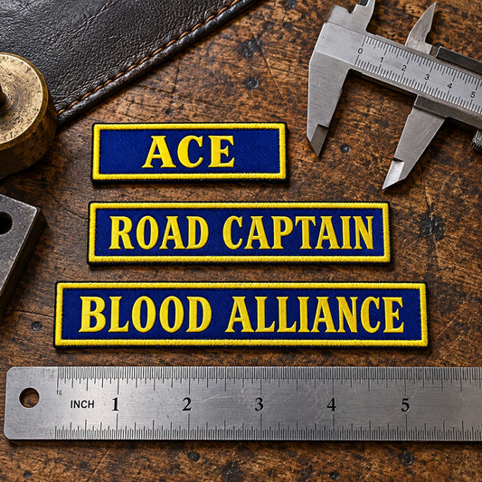Several true-scale custom-width name bars beside calipers and a ruler on a patch inspection table, with no hands present, showing custom motorcycle club name bar patch options.