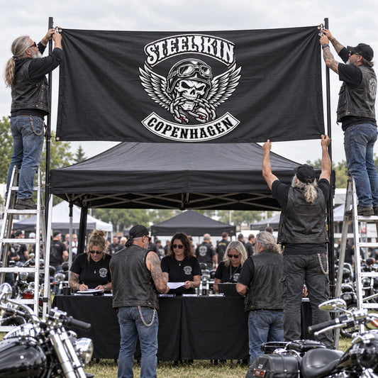Rally volunteers secure a wide custom motorcycle club flag above an outdoor registration tent.