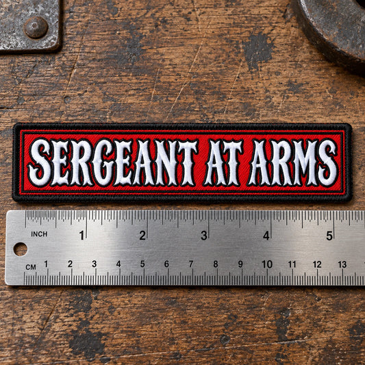 Large 5 by 1.25 inch officer-title name bar with comfortable letter spacing beside a precise metal ruler on leather, showing custom motorcycle club name bar patch options.