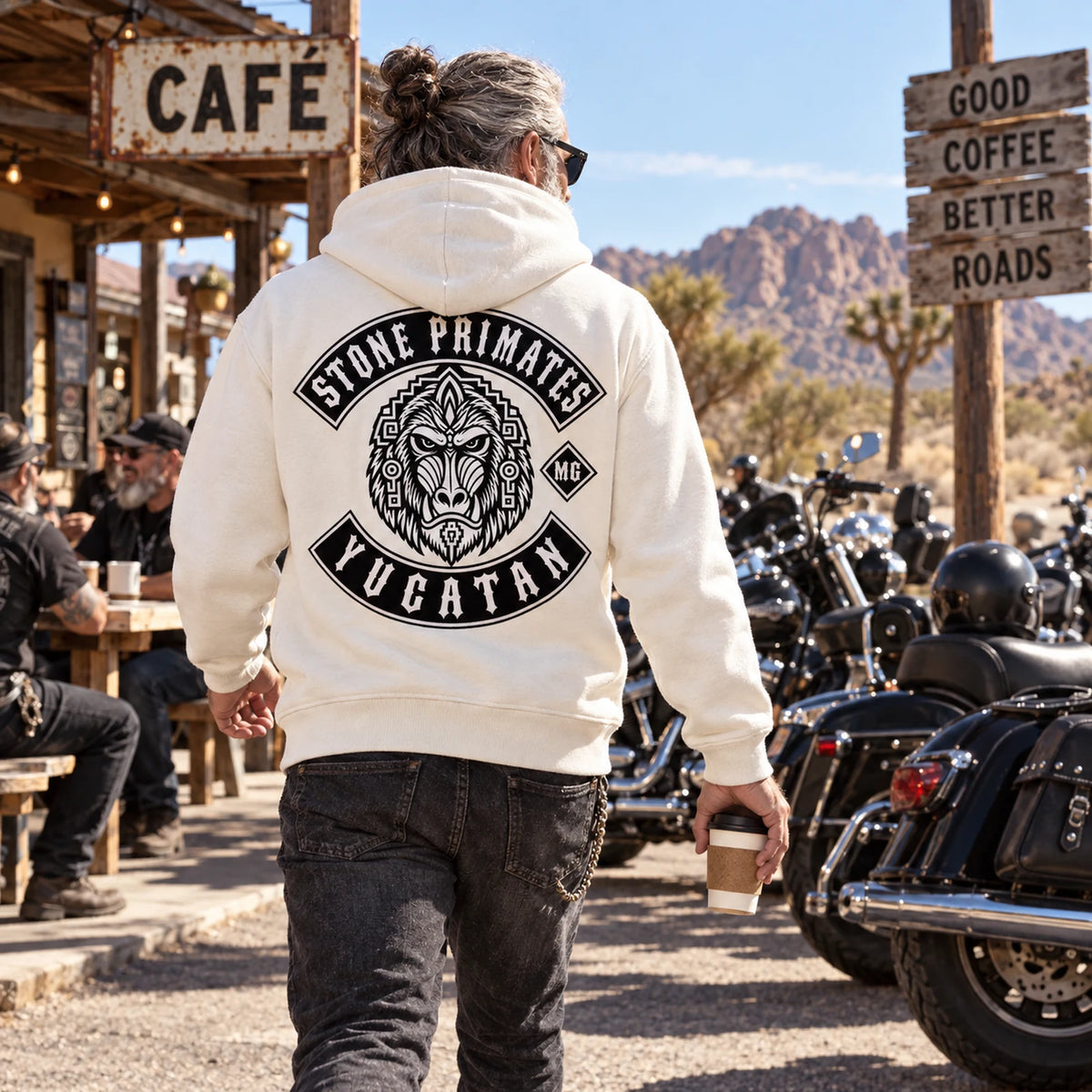 Rider wearing an off-white custom motorcycle club hoodie at a sunlit desert-road cafe.