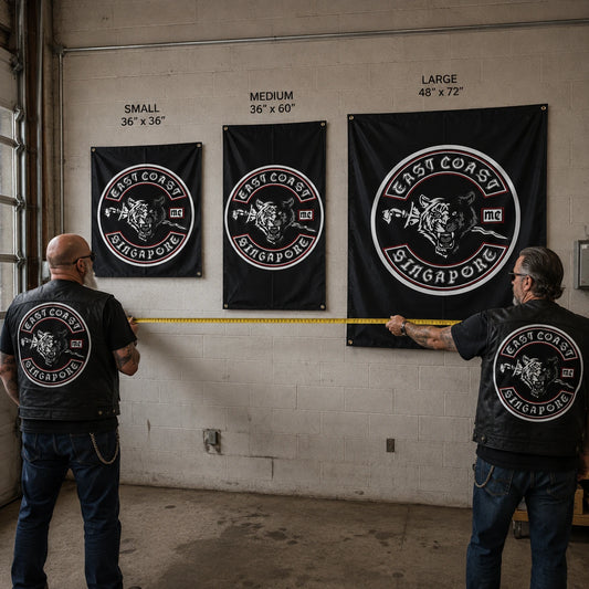 Two motorcycle club members measure a garage wall while comparing three custom hanging flag sizes.