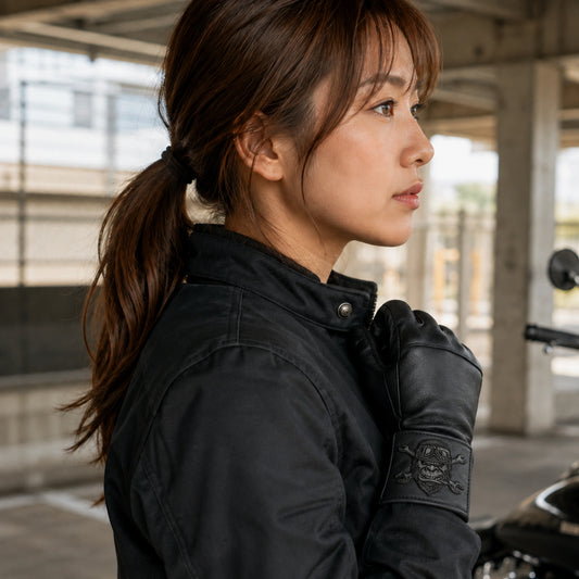 Short-cuff black leather club gloves carry a thin sewn leather patch beside a riding jacket sleeve.