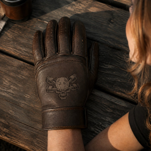 A brown motorcycle club glove carries a dark laser-engraved emblem within the lower back-of-hand panel.