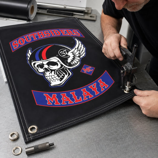 A craftsperson adding reinforced edges and grommets to a custom club event banner.