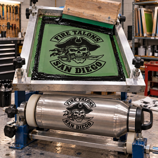 one-color screen-print production applying a faithful simplified monochrome version of the exact supplied logo to a stainless bottle, photographed in a complete rectangular workshop scene whose background fills every edge and corner for a motorcycle club.