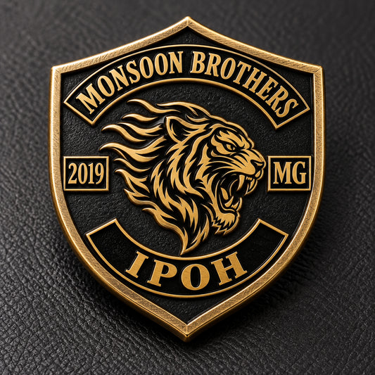 Antique bronze shield-shaped MONSOON BROTHERS pin with a sculpted tiger and clearly defined outer rim on black leather.