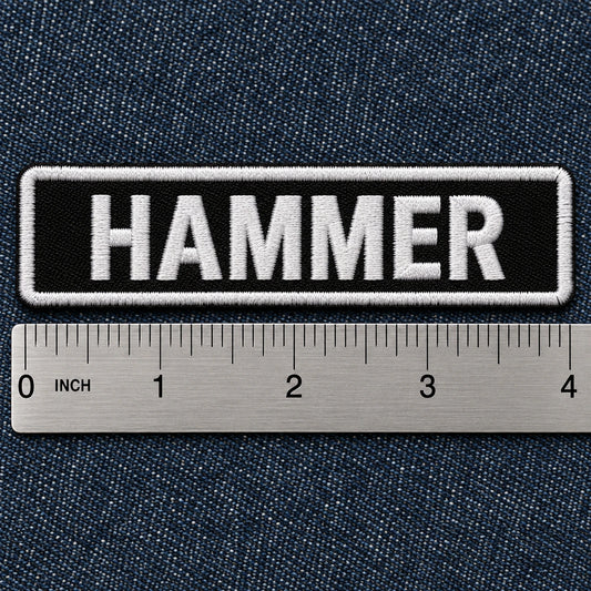 Standard 4 by 1 inch motorcycle name bar beside a precise metal ruler on dark denim for clear scale, showing custom motorcycle club name bar patch options.