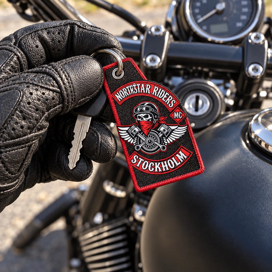 Lightweight custom motorcycle club key tag with an authorized logo held above a parked motorcycle cockpit.