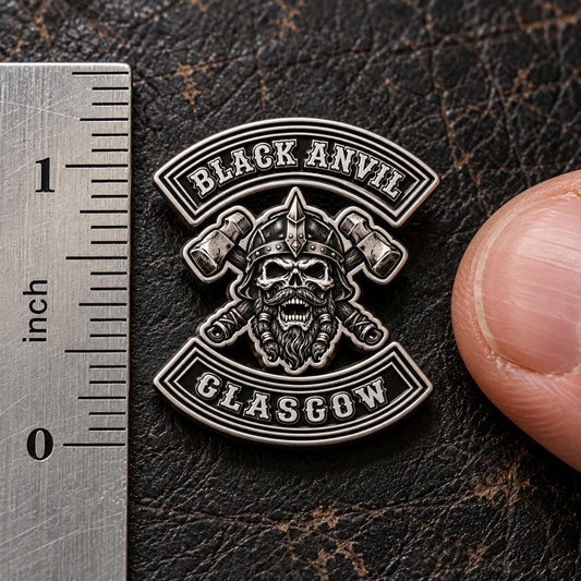 Compact one-inch BLACK ANVIL sculpted club pin beside an imperial ruler and fingertip.