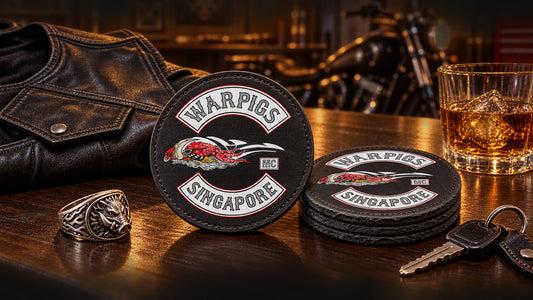 Custom motorcycle club coasters beside a leather vest, ring and keys on a clubhouse bar.