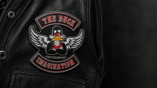 One-piece custom motorcycle club enamel pin on a continuous solid metal base displayed on a black leather vest.