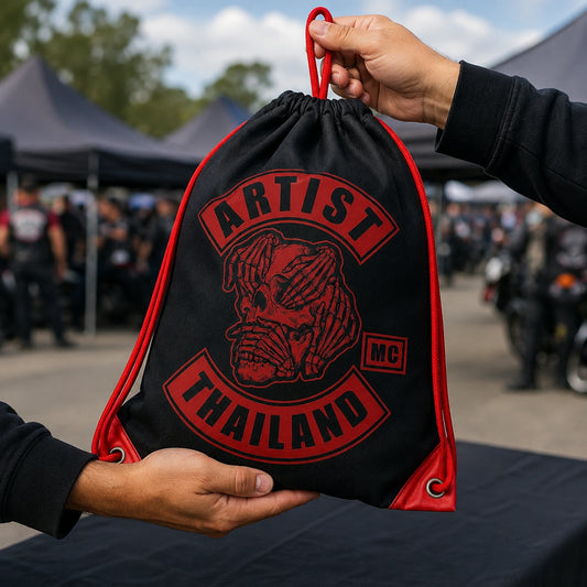 Two riders exchange an official Artist MC drawstring bag at an annual motorcycle club rally registration table.