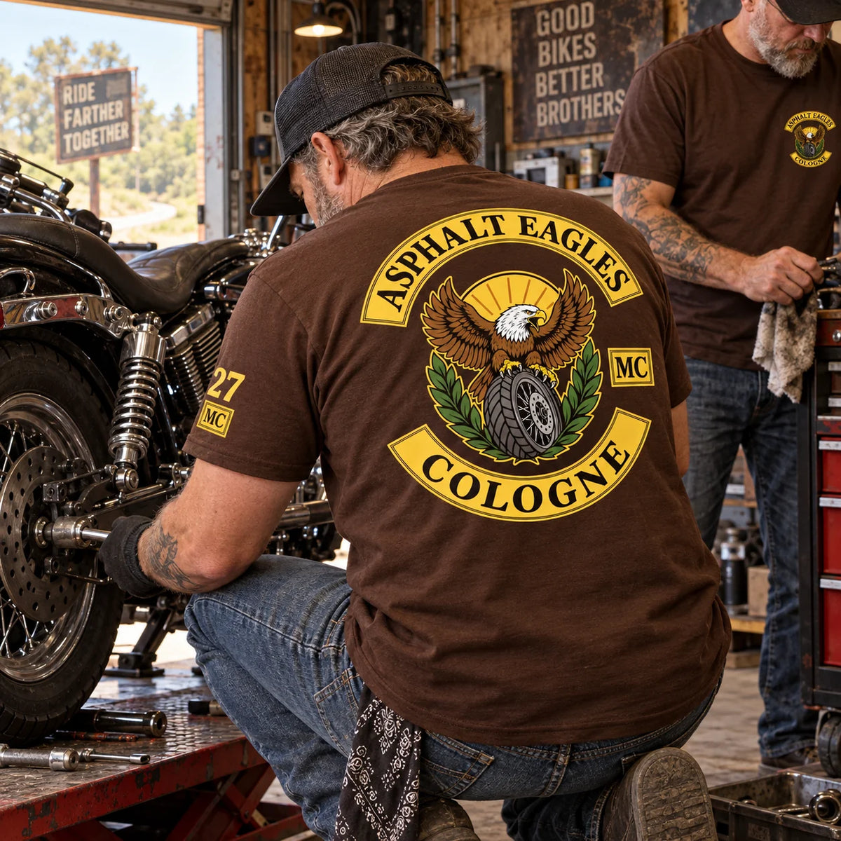 Asphalt Eagles Cologne member wearing a brown club T-shirt with a small number 27 sleeve print while working on a motorcycle in a roadside garage.