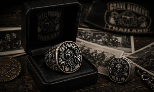 Limited edition custom motorcycle club anniversary ring displayed in a black leather presentation box with vintage club photos and an older matching ring on a dark clubhouse table.