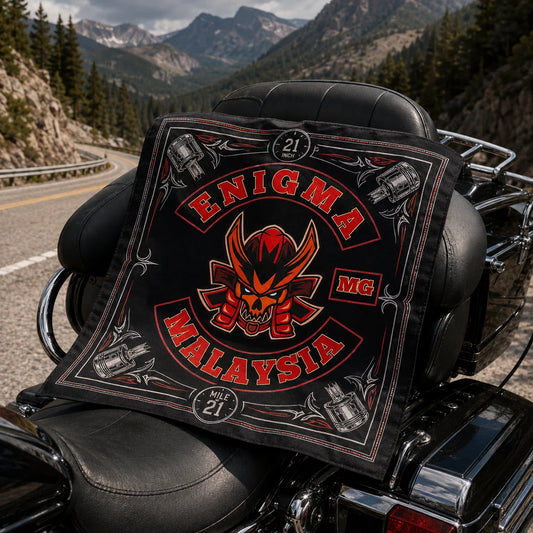 Custom motorcycle club bandana featuring the authorized Enigma MG Malaysia identity in classic bandana laid across a touring motorcycle seat with a ruler and mountain road in the distance.