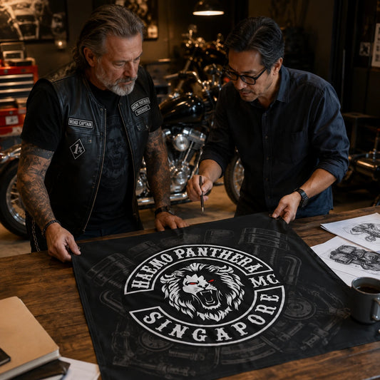 A club road captain reviews V-twin-inspired custom flag artwork with a designer beside the workshop.