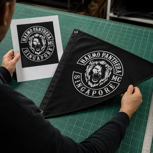 A print technician compares approved motorcycle club artwork with the finished custom triangle flag.