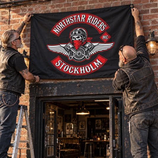 Two motorcycle club officers mount a custom chapter flag at a brick clubhouse entrance.