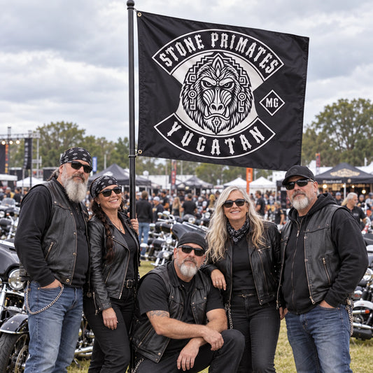 Motorcycle club riders gather around a tall custom event flag at a busy outdoor V-twin rally.