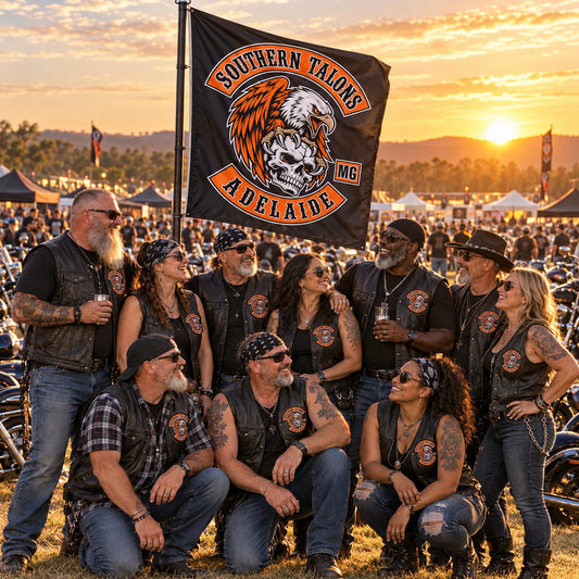 A large motorcycle club group gathers around its custom flag at a golden-hour regional V-twin rally.