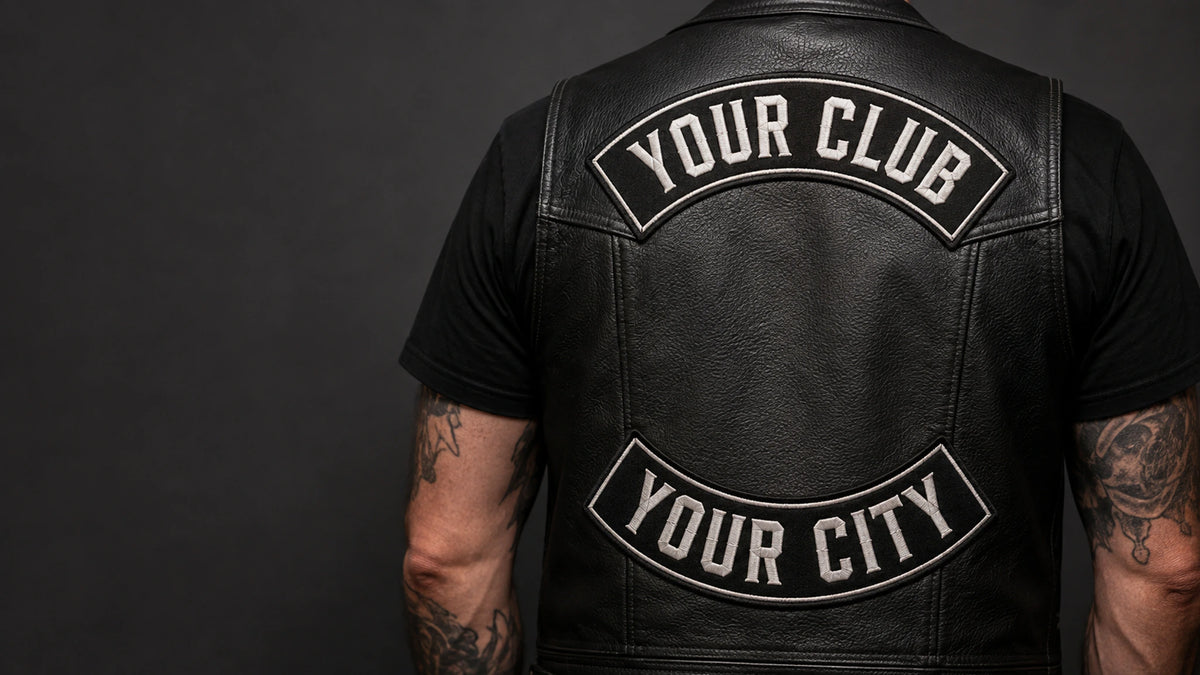 Custom motorcycle club top and bottom rocker patches arranged on the back of a black leather riding vest.