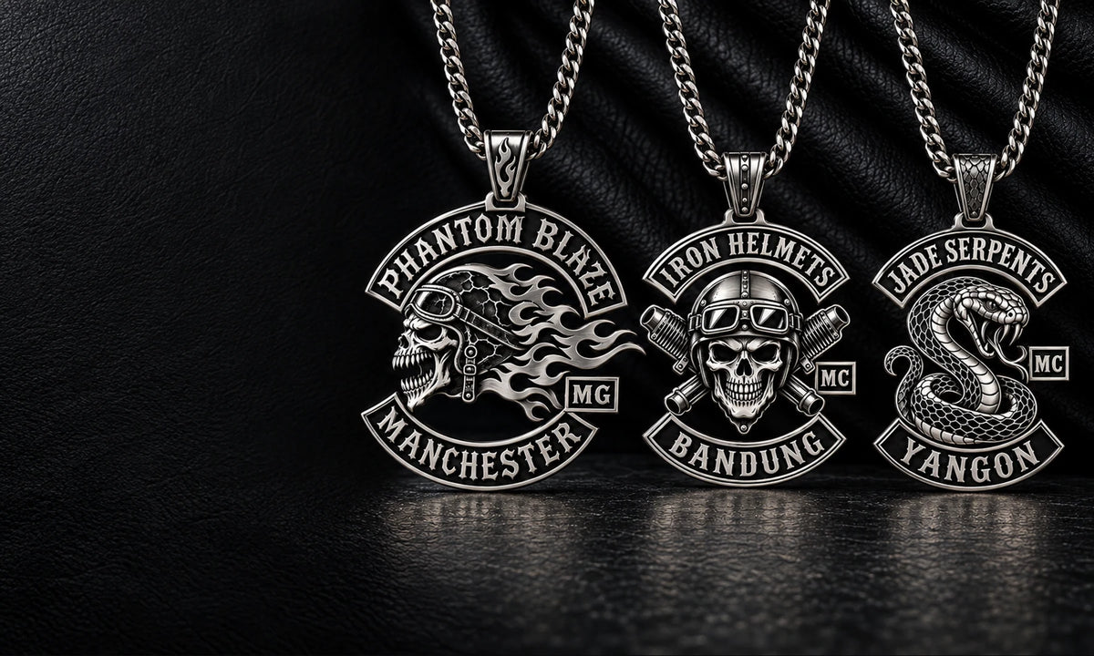 Three custom stainless steel motorcycle club pendants with unique sculptural emblems in a dark jewelry studio.