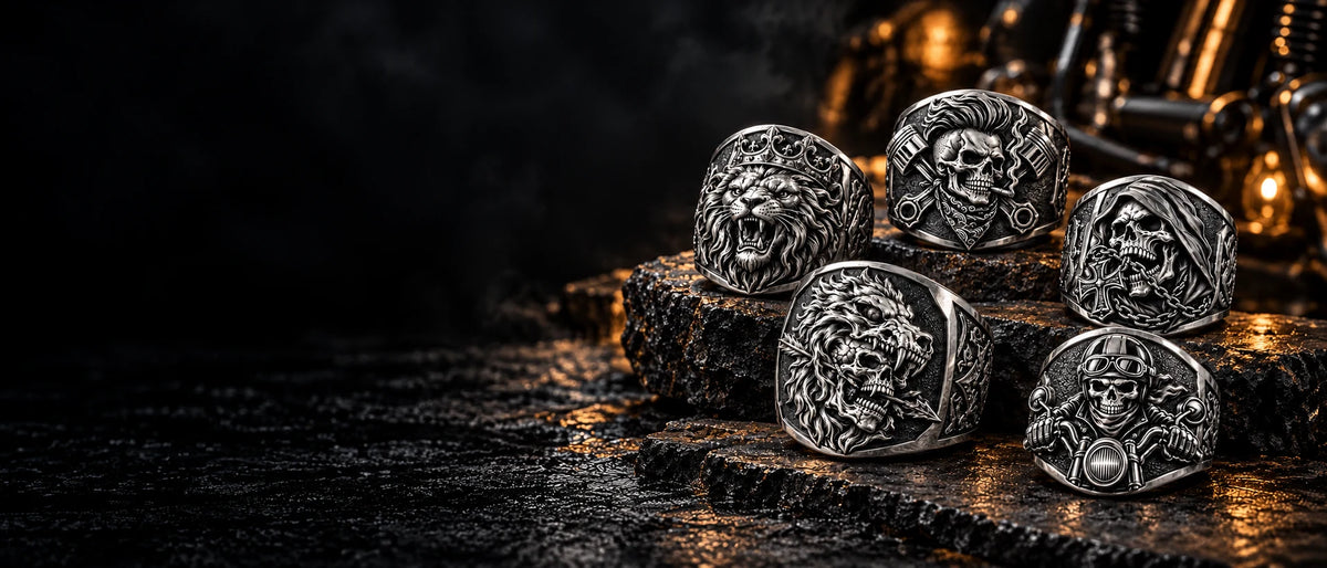 Five custom white copper motorcycle club rings featuring distinct wolf, crowned lion, skull, chain and biker emblems in a dark jewelry studio.
