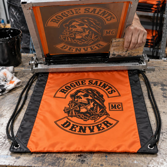 An orange and black two-tone polyester motorcycle club drawstring bag receives a bold screen print.