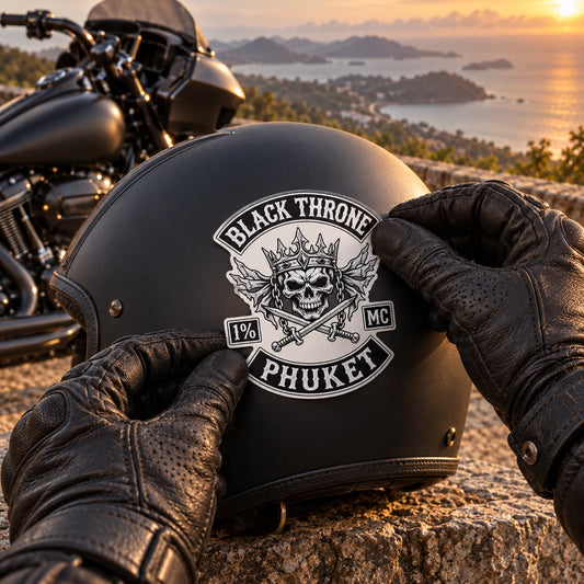 Gloved rider applying a contour-cut motorcycle club logo sticker to a matte black helmet beside a V-twin motorcycle.