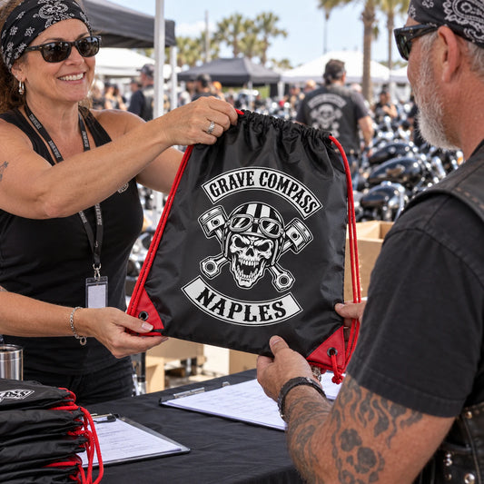 Two riders exchange an official Artist MC drawstring bag at an annual motorcycle club rally registration table.