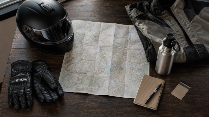 Motorcycle trip planning flat lay with map, gloves, notebook, weather layers and safety equipment