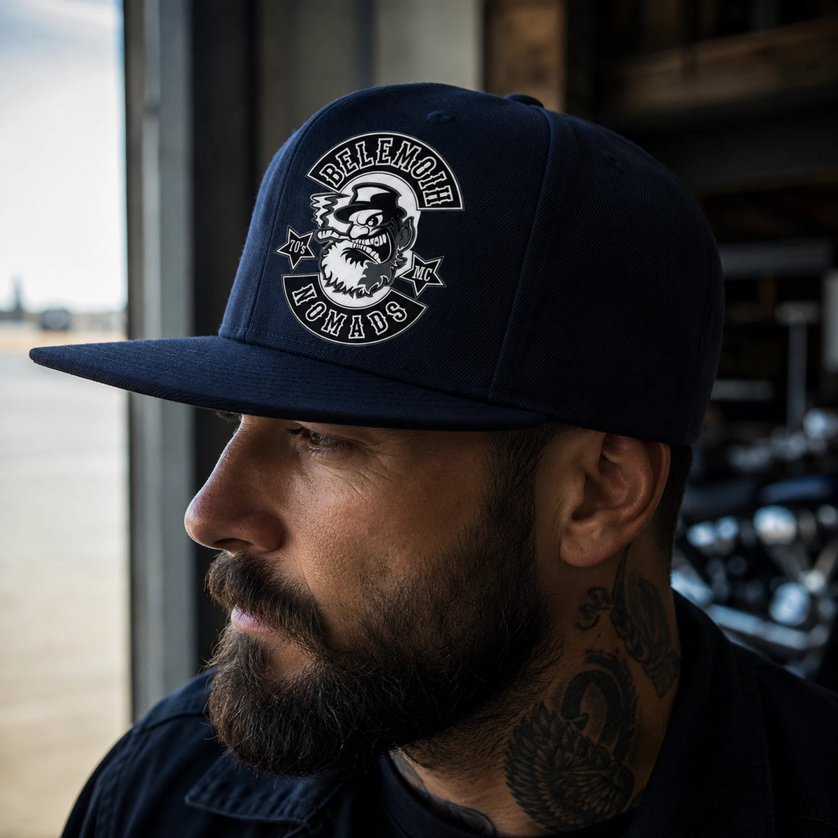 A motorcycle club rider wears a streamlined navy fitted flat-brim cap with an approved emblem.
