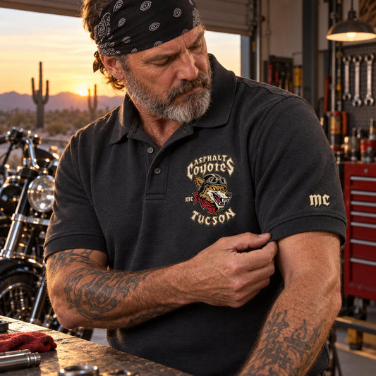 A mechanic examines a heavyweight charcoal Asphalt Coyotes Tucson club polo in a V-twin service garage.