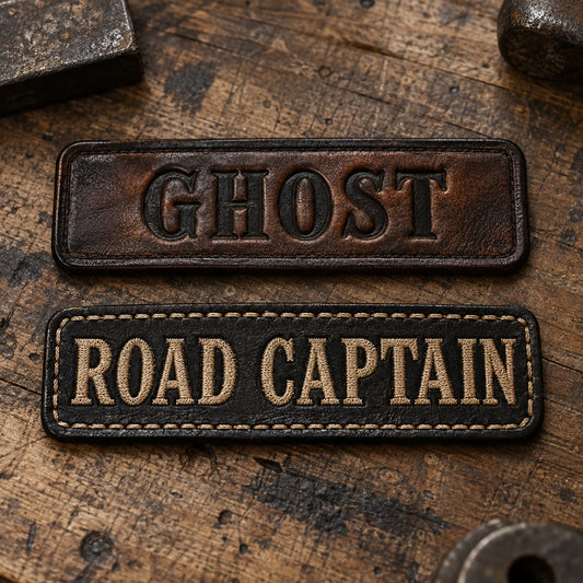Premium embossed and stitched leather motorcycle club name bars arranged on a worn wooden workbench, showing custom motorcycle club name bar patch options.