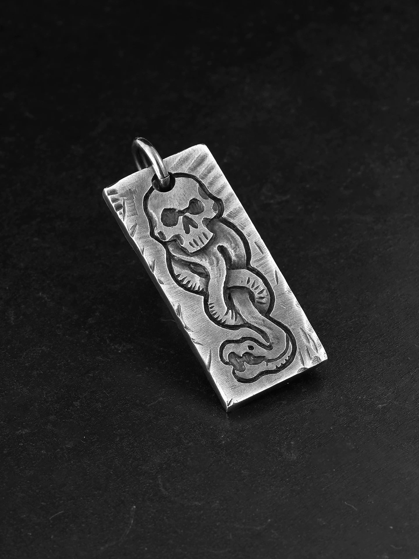 Angled view of handcrafted skull and snake silver dog tag pendant