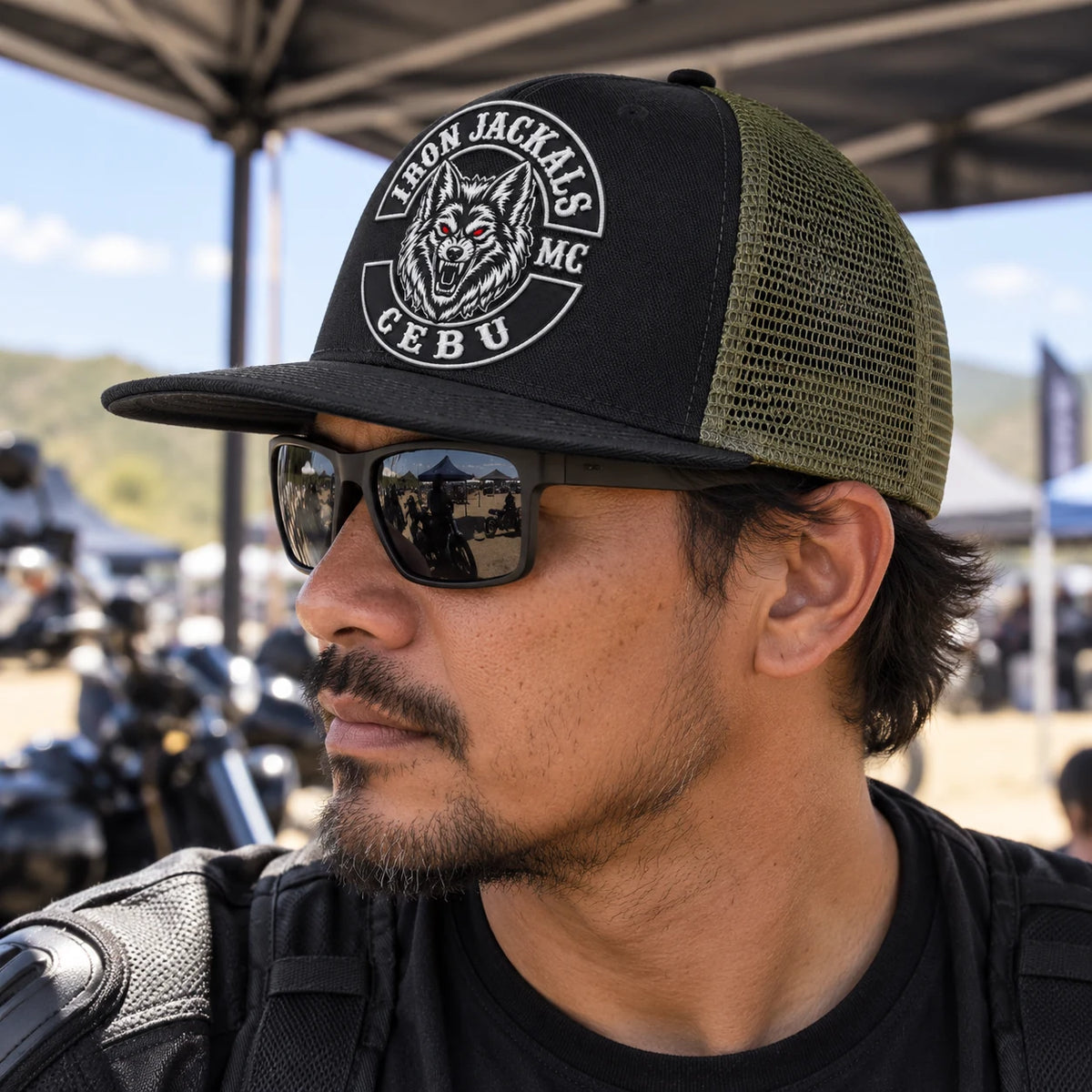 Un motociclista de club lleva una gorra de ala plana con una parte delantera estructurada y una parte trasera de malla transpirable de color verde oliva.